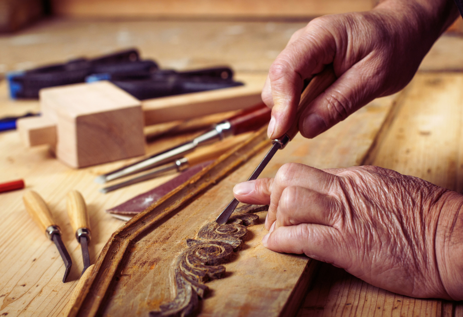 Hands holding a sharp pointed tool to carve a design into a piece of wood